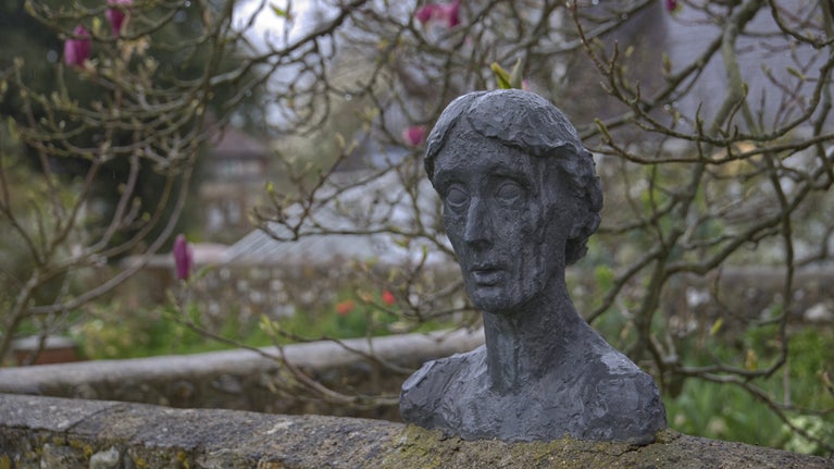 A bust statue of Virginia Woolf on a wall in a garden